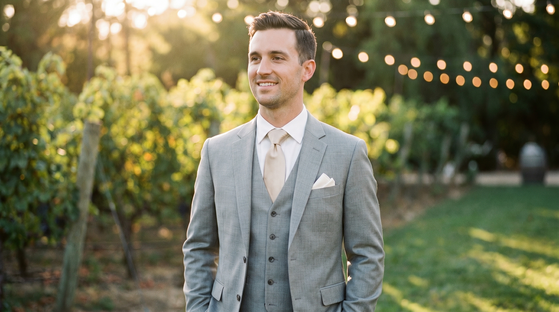 Elegant groom in a light gray suit and champagne silk tie at an outdoor wedding